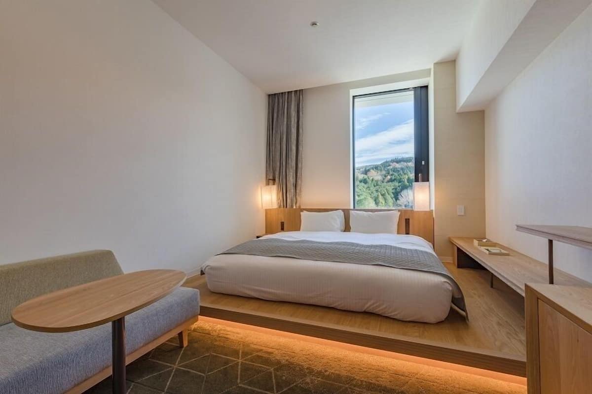 Ein modernes Hotelzimmer mit Bett, einer Sitzecke und einem Fenster mit Blick auf die Stadt.