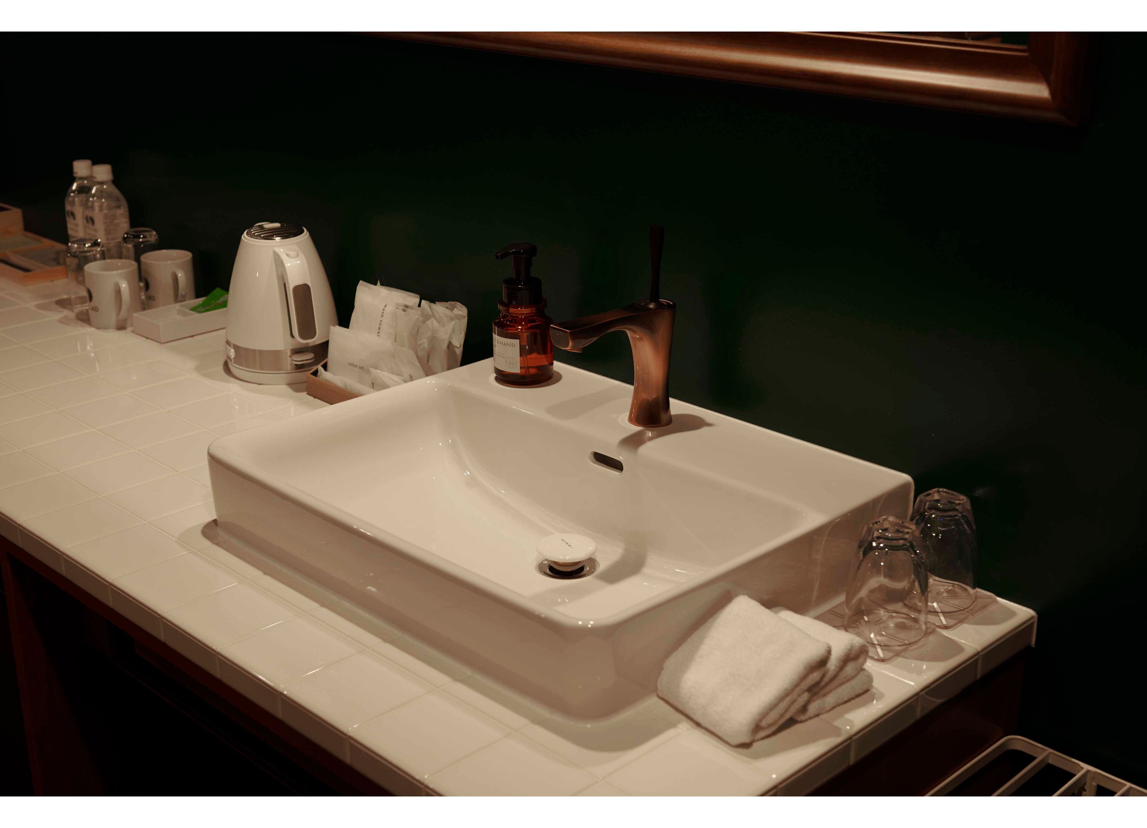 A hotel bathroom with a white sink, a bottle of hand soap, a towel, and a glass.