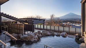 Un onsen japonés tradicional con una terraza de madera, rocas grandes y vistas a la montaña.