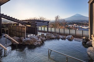 Uma onsen japonesa tradicional com um deque de madeira, pedras grandes e vista para uma montanha.