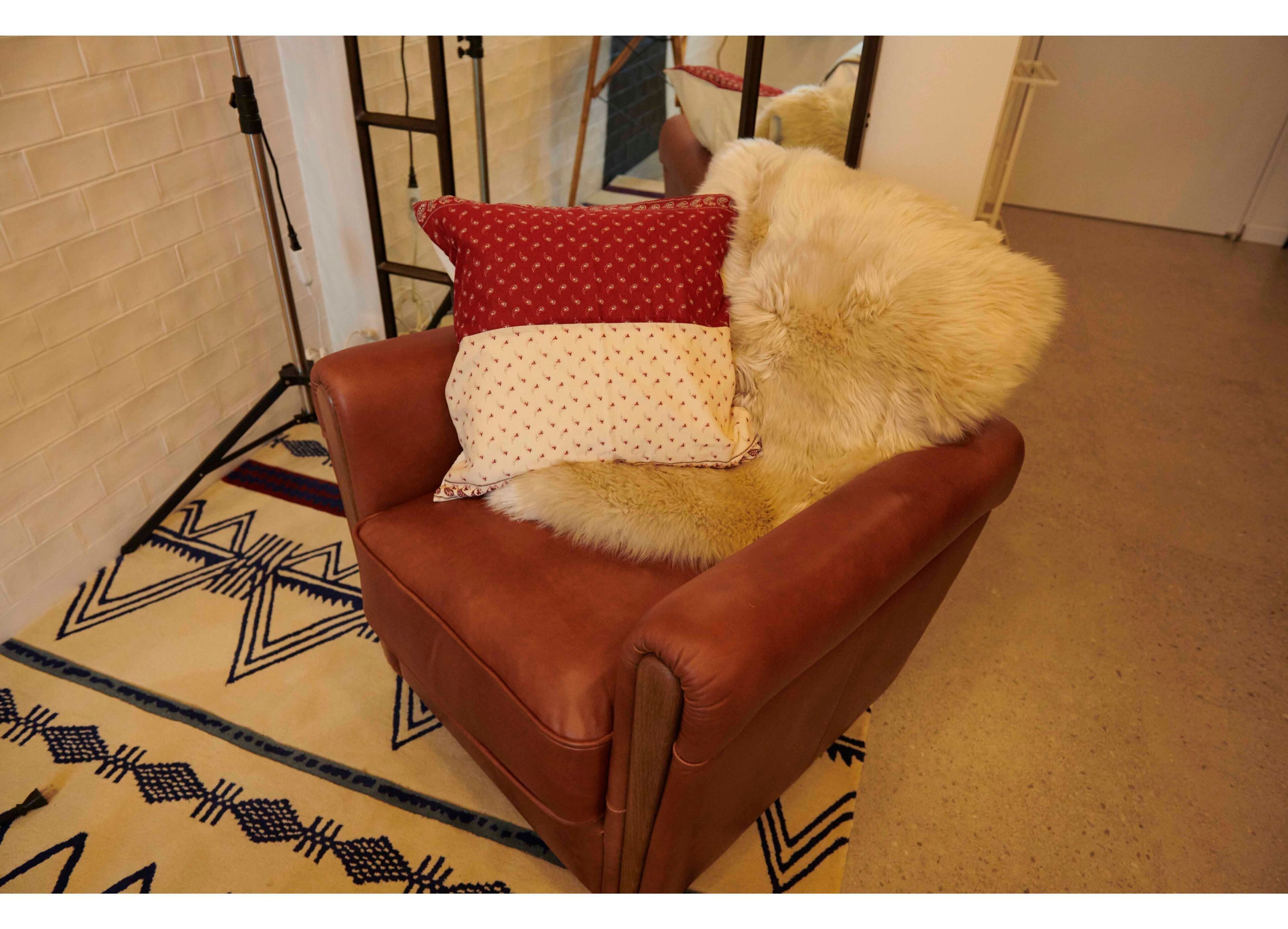 Un fauteuil en cuir marron agrémenté d’un coussin décoratif à motifs et d’un coussin moelleux blanc.