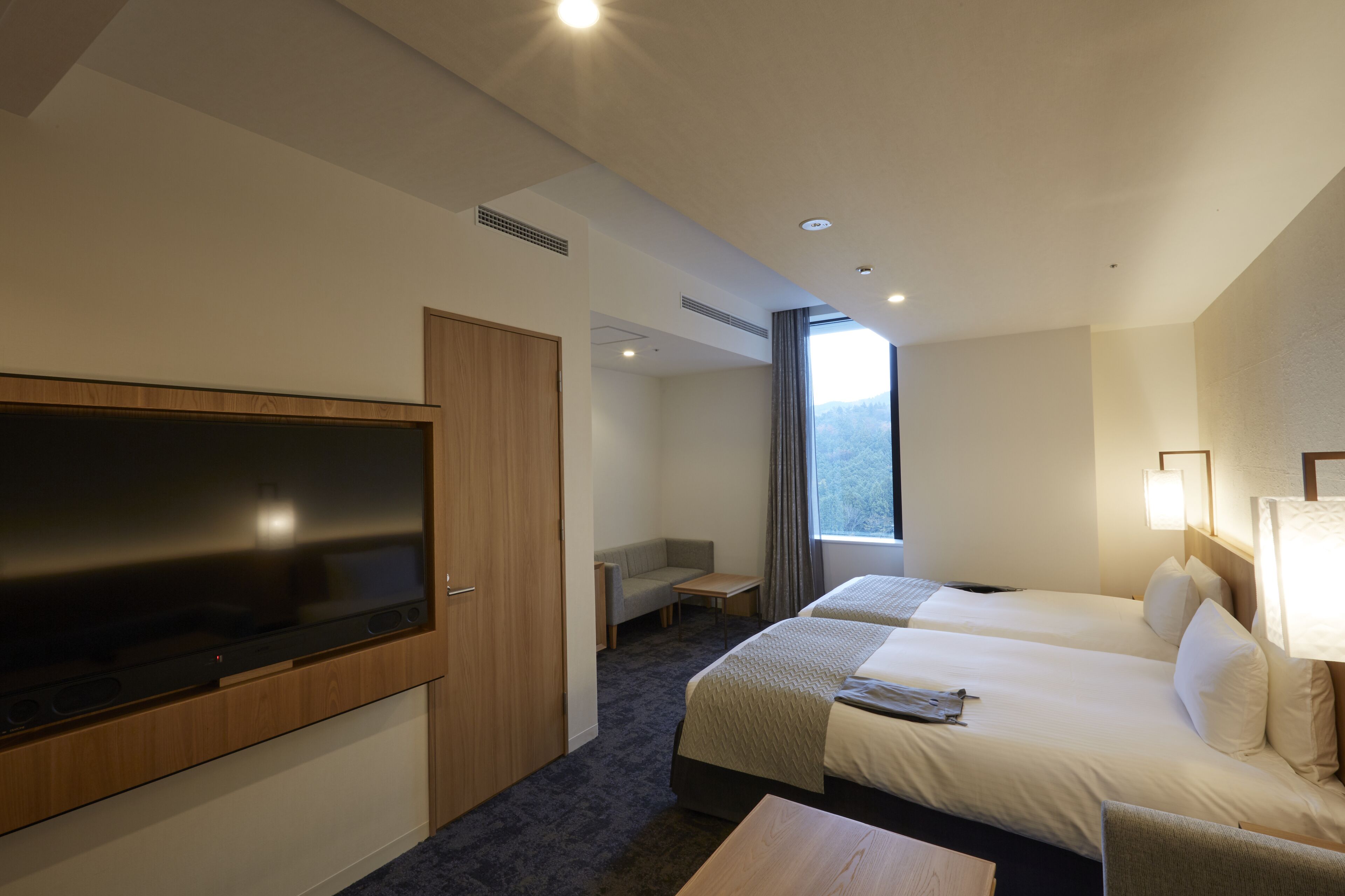 A hotel room with a flat-screen TV, two beds, a desk, and a window with a view.