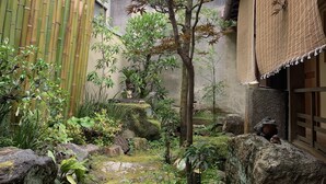 A traditional Japanese garden with a bamboo fence, a small tree, rocks, and moss-covered ground. - Traditional Guesthouse TONARI (Nara)
