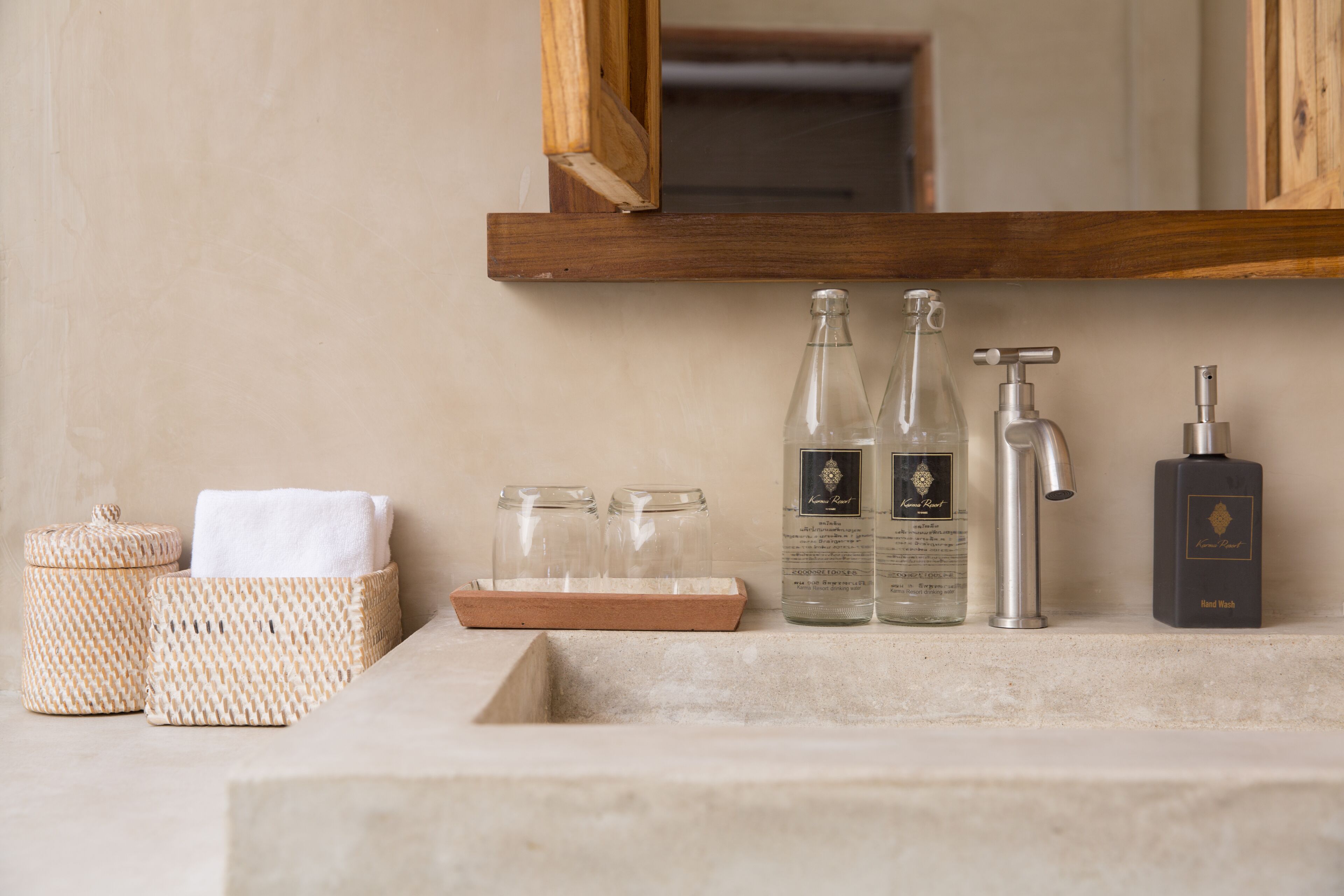 A bathroom vanity with a wooden shelf holding a white towel, two glass bottles, a silver faucet, and a black soap dispenser.