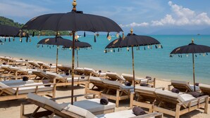 A beach with wooden lounge chairs and black umbrellas. - Karma Resort (Koh Samui)