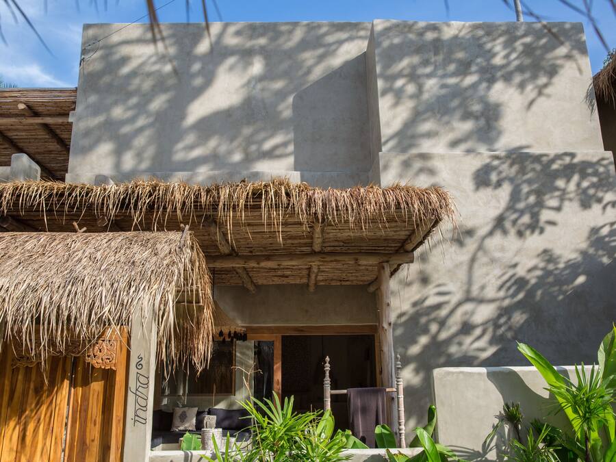 Un bâtiment doté d’un toit de chaume, d’une façade en béton et d’une porte en bois portant l’inscription « Indah ».