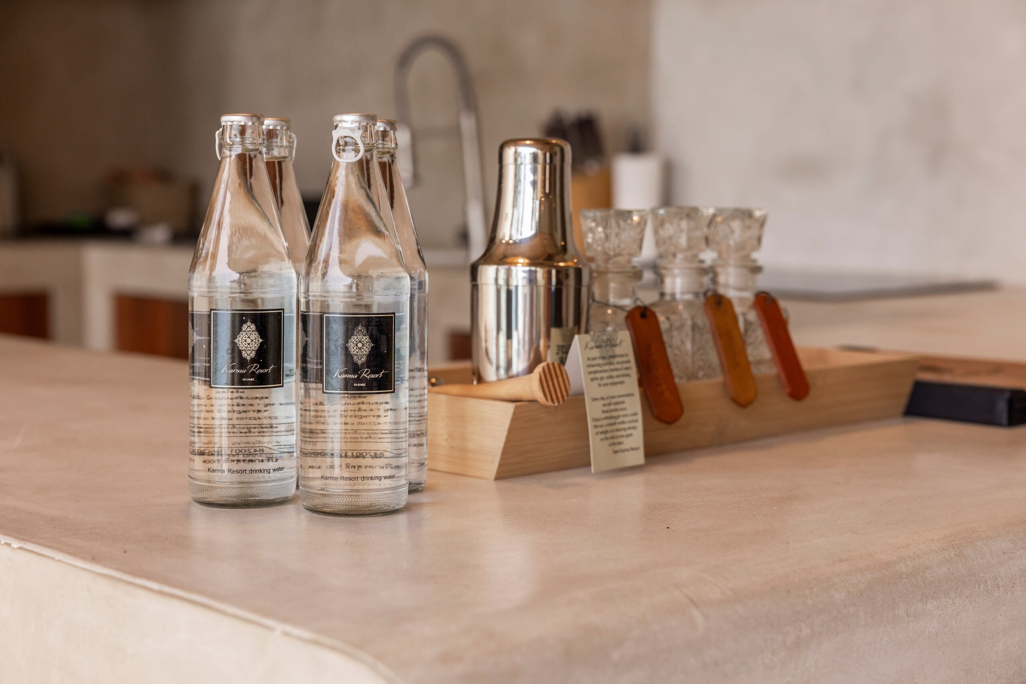 Drei Flaschen Kamma Resort Trinkwasser, ein silberner Cocktail-Shaker und ein Holztischchen mit Gläsern.