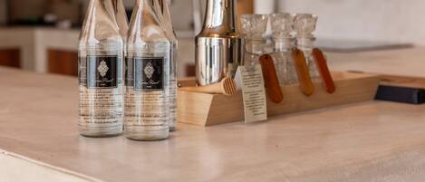 Tres botellas de agua del Kamma Resort, un batidor de cócteles plateado y una bandeja de madera con vasos.