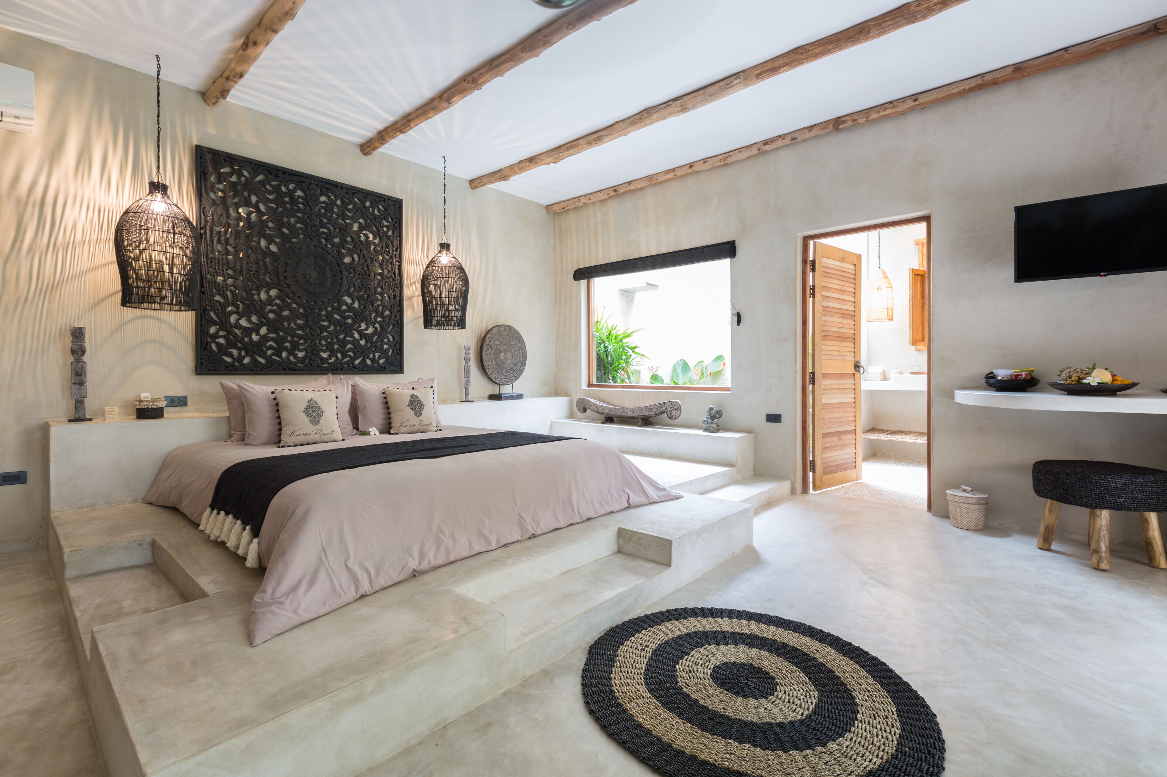 Une chambre à coucher avec un lit, une grande œuvre d’art murale, un téléviseur et une fenêtre donnant sur un paysage verdoyant.