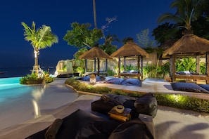 A beachfront resort with thatched-roof cabanas, lounge chairs, and a pool.