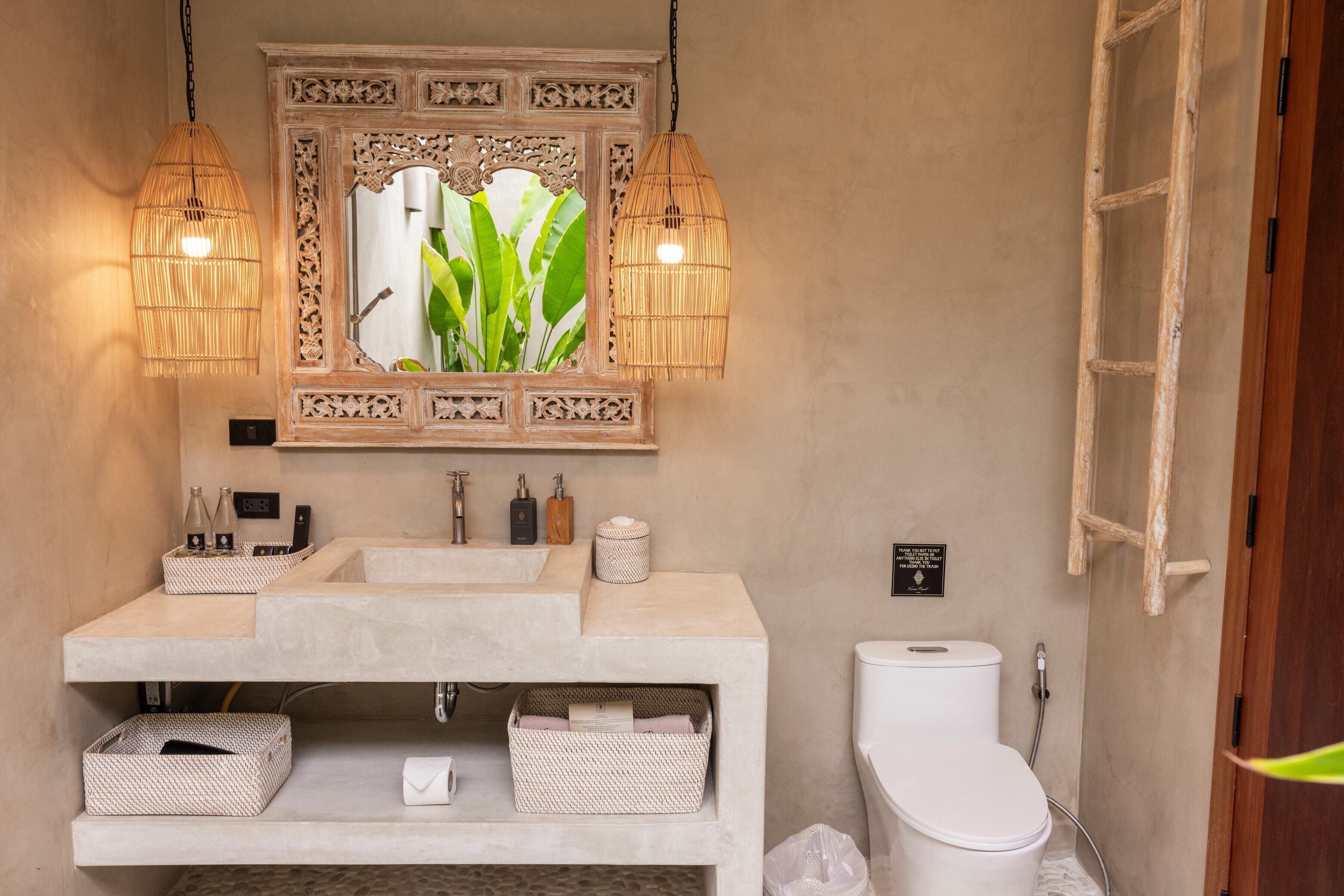 A bathroom with a large mirror, two pendant lights, a toilet, and storage baskets.