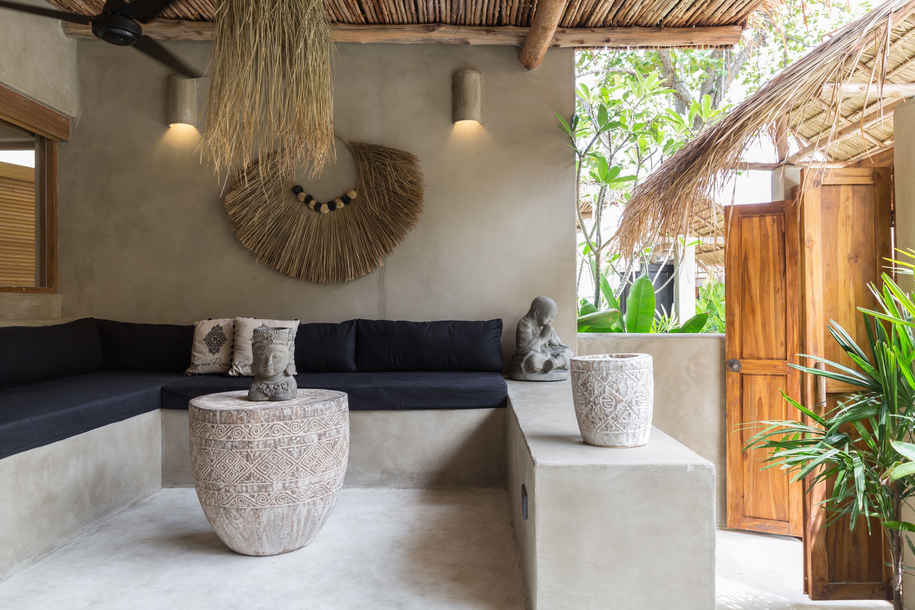 Een modern interieur met een donkere bank, twee decoratieve stenen plantenbakken, een geweven wanddecoratie en een houten deur.