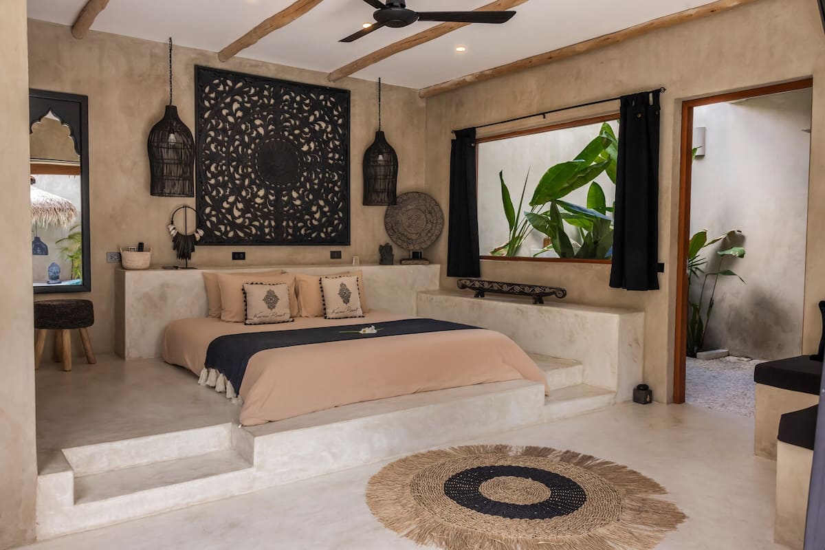 A bedroom with a bed, a large window, and a view of plants.