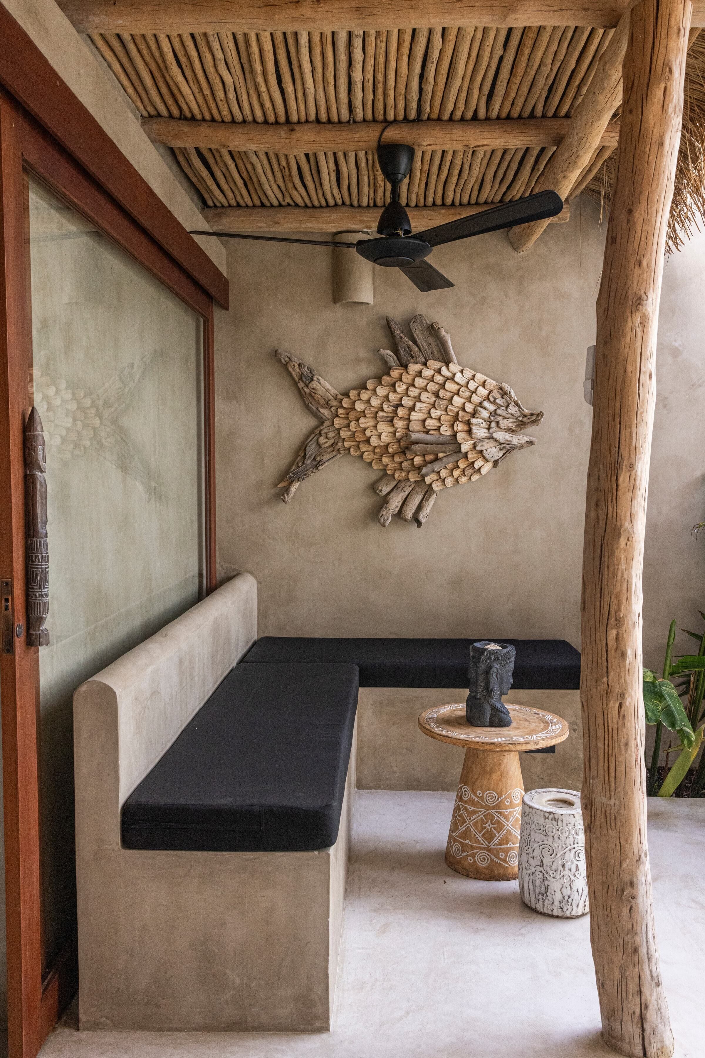 A room with a wooden ceiling, a wall-mounted fish sculpture, a bench, a small round table, and a decorative vase.