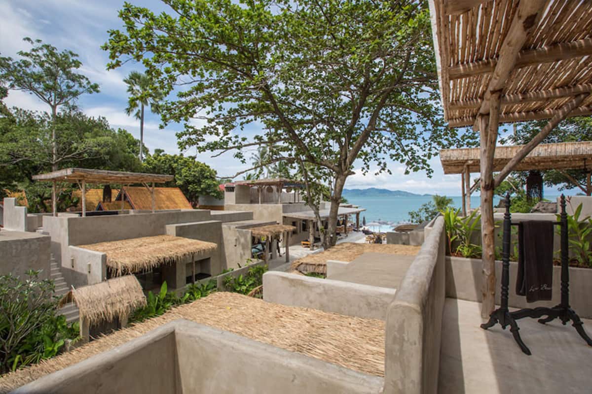 A resort with concrete structures, thatched-roof huts, and a view of the sea.