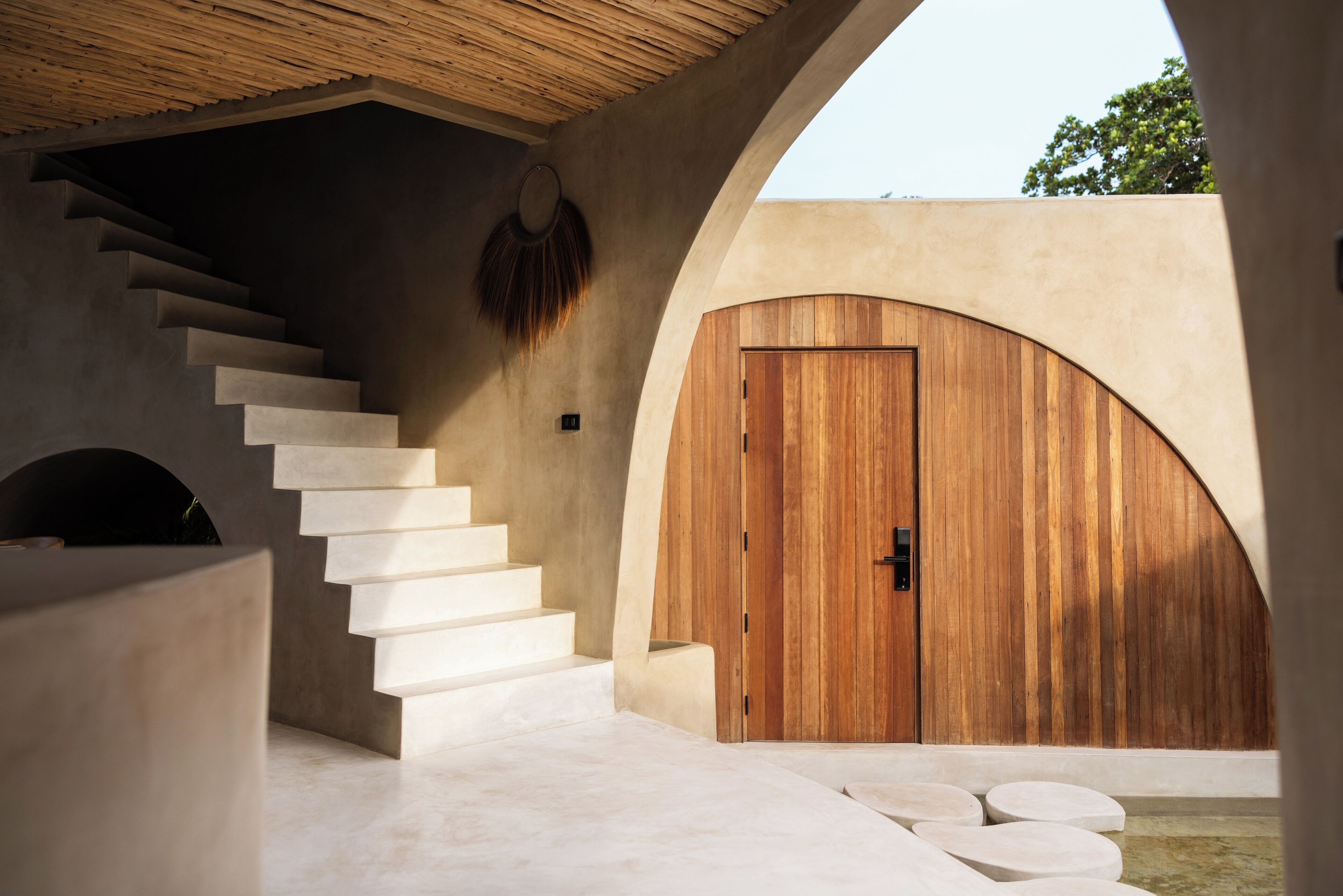 A modern interior with a staircase leading to a wooden door, a concrete wall, and a circular seating area.