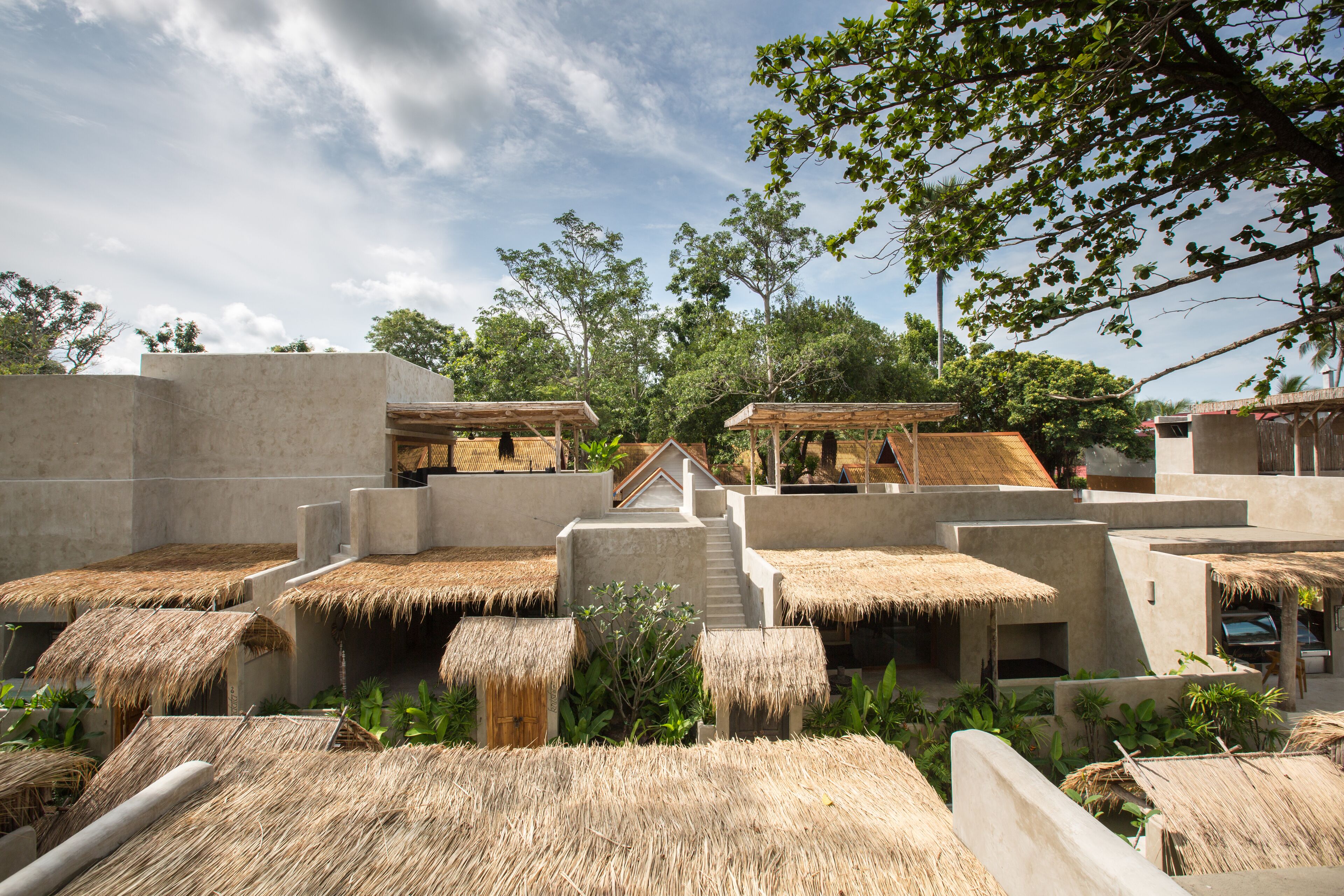 Un resort con cabañas de techo de paja, construcciones de concreto y exuberante vegetación.