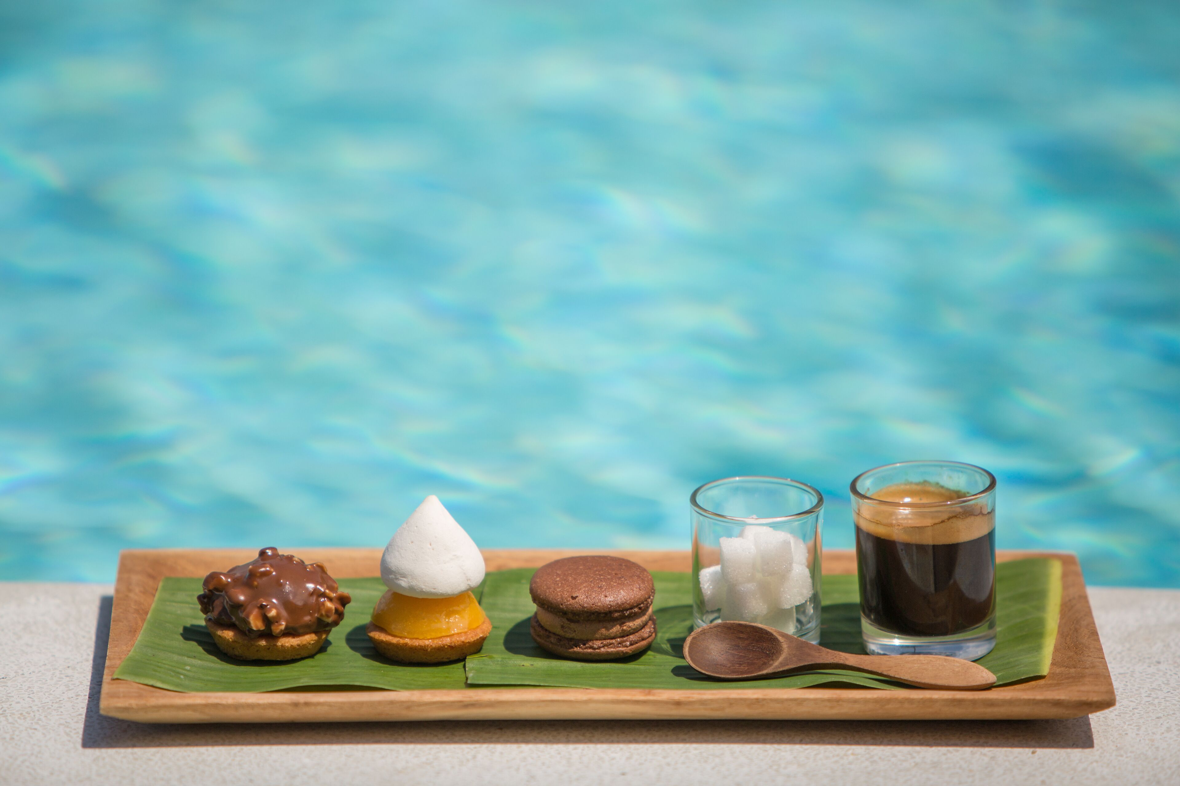A tray with desserts and drinks by a pool.