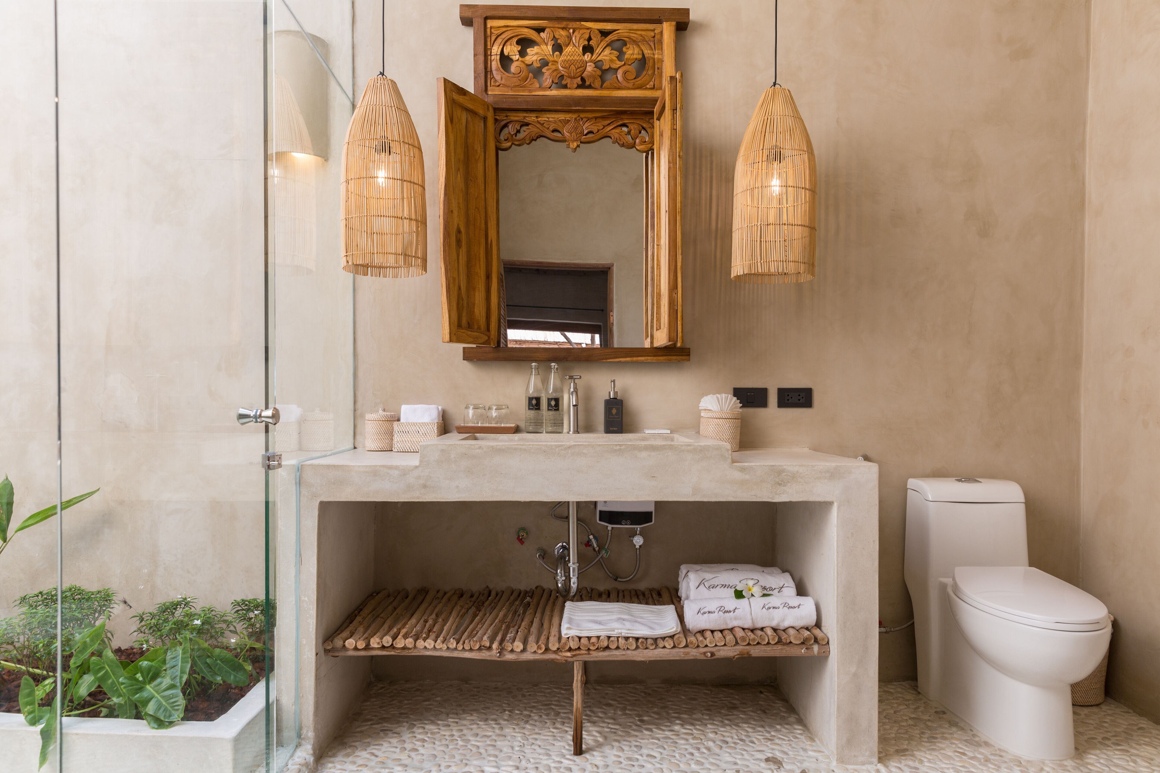 Un baño con cabina de vidrio, un estante de madera, un inodoro y un espejo con marco de madera.