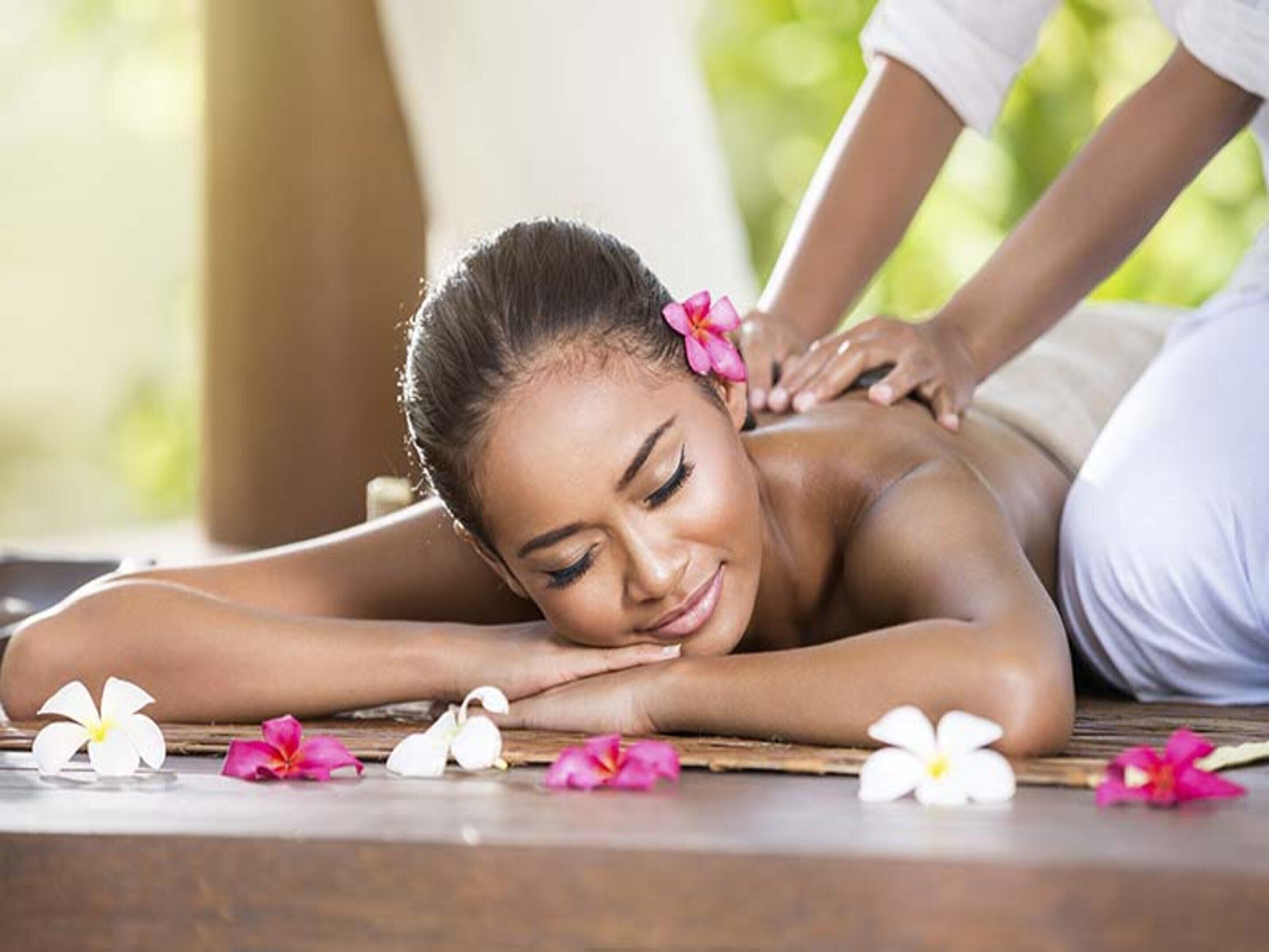 A person receiving a back massage on a wooden floor with flowers.