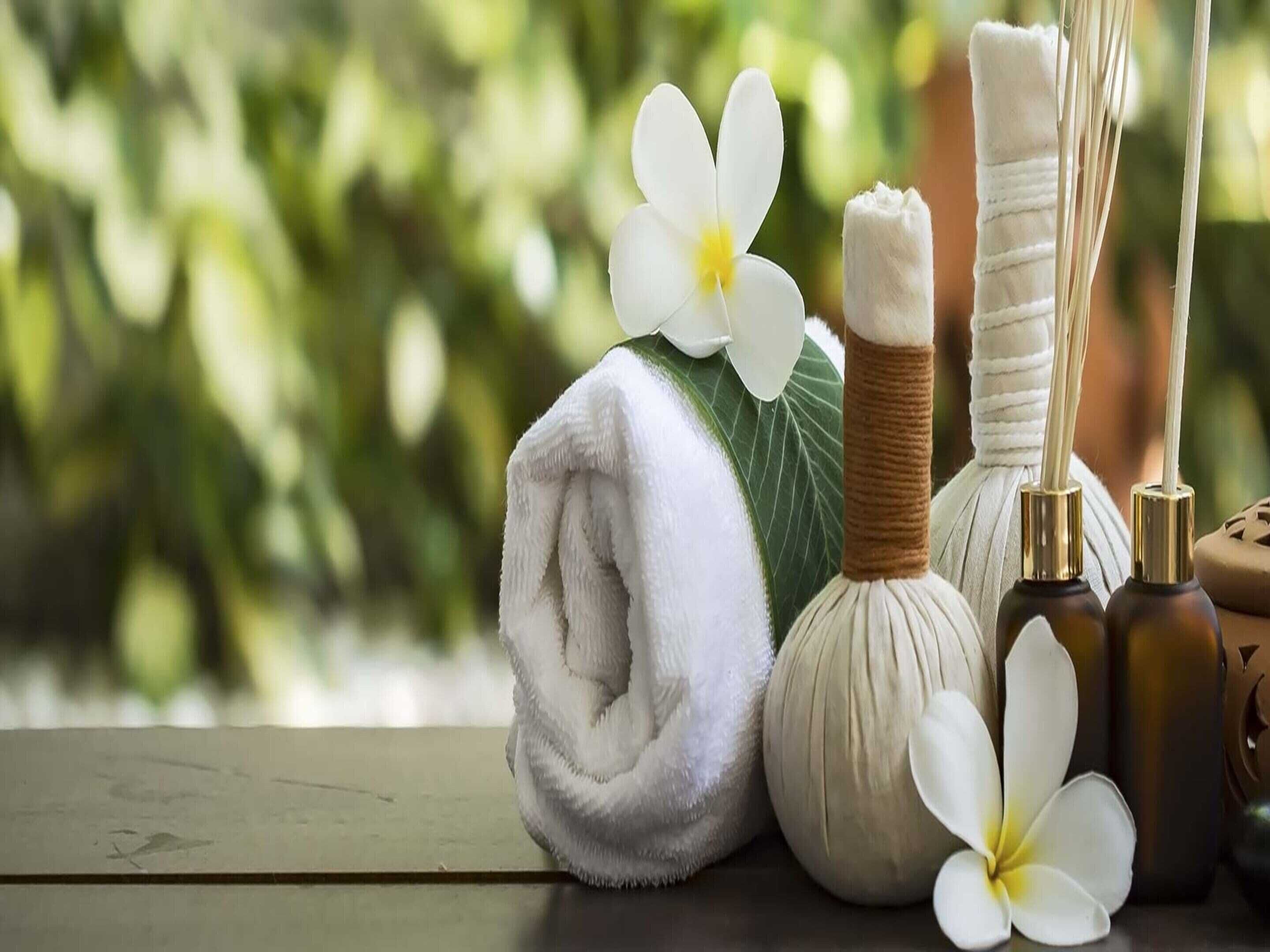 A towel, a massage oil bottle, and a flower on a wooden surface with a blurred green background.