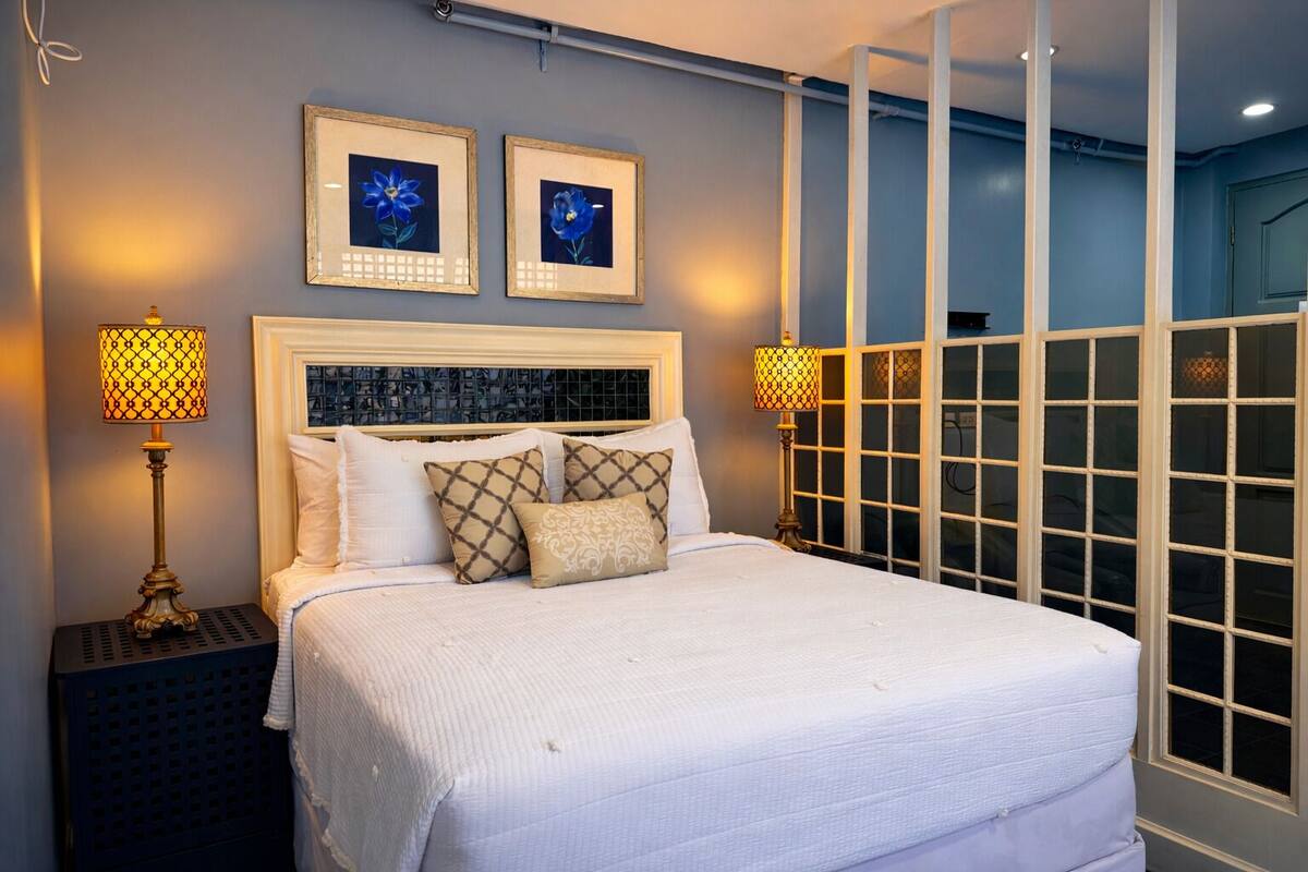 Een bed met een wit hoofdeinde, twee ingekaderde foto's erboven en twee bedlampjes.