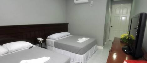 Una habitación de hotel con dos camas, un escritorio con computadora, teléfono y televisión.