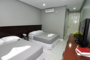 Una habitación de hotel con dos camas, un escritorio con computadora, teléfono y televisión.
