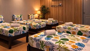 Een hotelkamer met vier bedden, elk voorzien van een bloemenprint beddegoed, een wandairconditioner, een potplant en een deur.