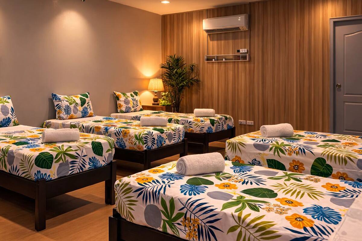 Een hotelkamer met vier bedden, elk voorzien van een bloemenprint beddegoed, een wandairconditioner, een potplant en een deur.