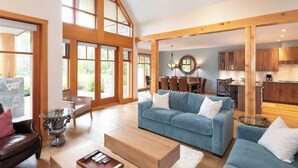 A spacious living room with a blue sofa, wooden dining table, and large windows. - Family-friendly townhouse w/ hot tub (Whistler)
