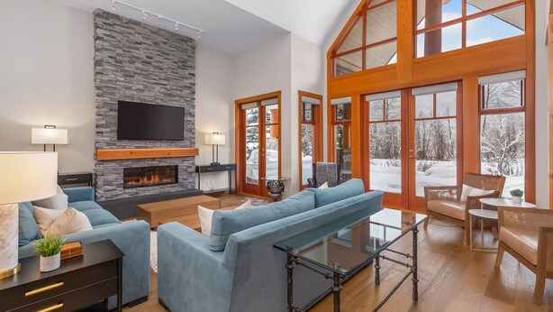 A spacious living room with a stone fireplace, a large TV, and a high ceiling with wooden beams. - Family-friendly townhouse w/ hot tub (Whistler)