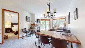 A spacious room with a wooden dining table, multiple chairs, a sofa, and a television. - Aspens #332 2-Bedroom Ski in Ski out, sleeps 6, Free Wifi (Whistler)