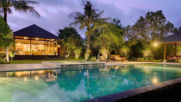 A pool area with a house in the background, surrounded by lush greenery and palm trees. -  Ketewel Villa by Sanga Sanga Hospitality (Sukawati)