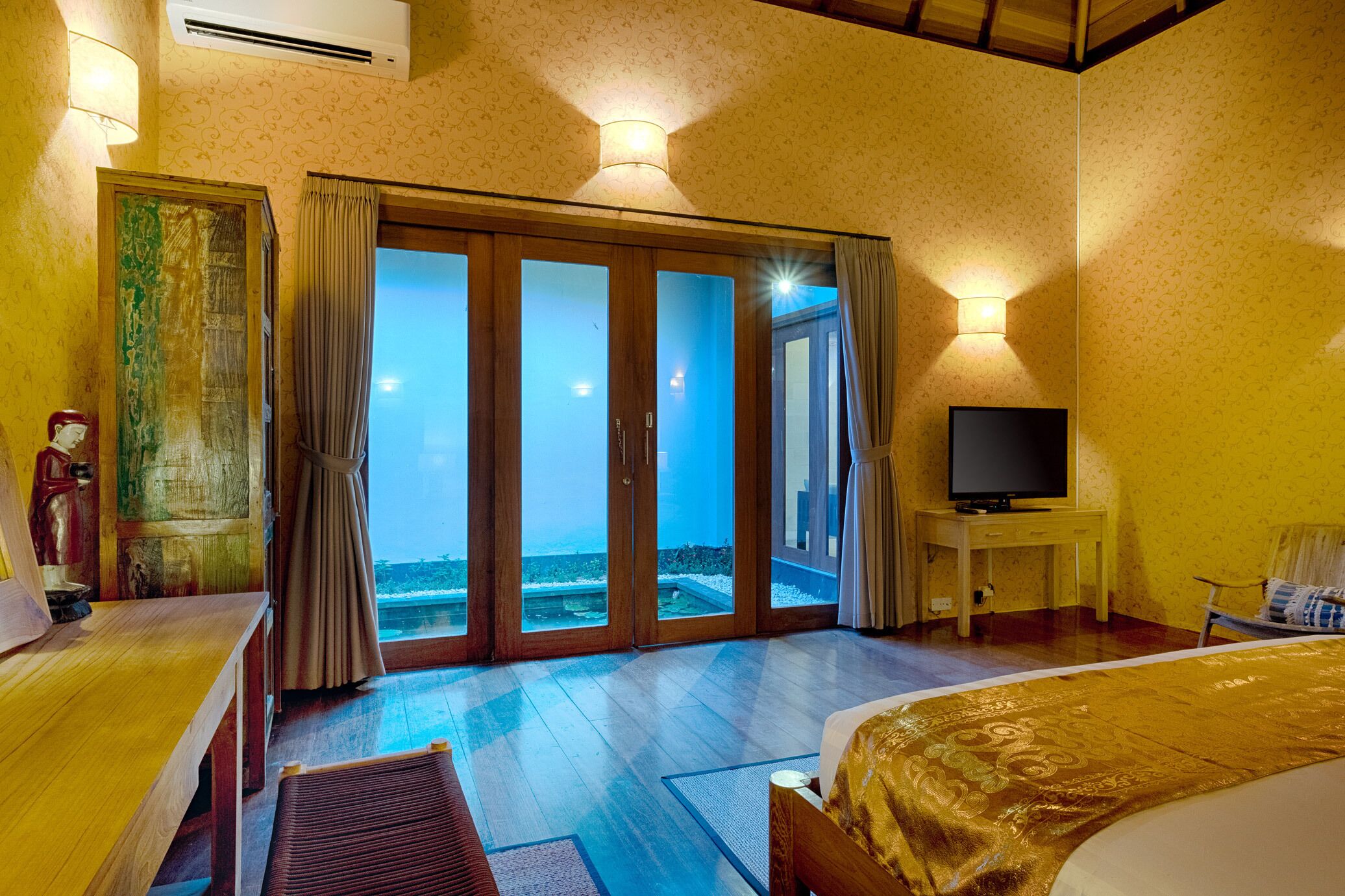 A hotel room with a large sliding glass door leading to a balcony, a bed, a television on a small table, and a lamp.
