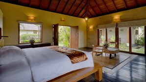A bedroom with a bed, a wooden bench, and a table with chairs. There are windows and doors leading to a balcony. -  Ketewel Villa by Sanga Sanga Hospitality (Sukawati)