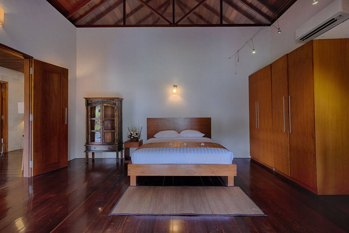 Een slaapkamer met een houten bed, nachtkastje, kast en plafondventilator.