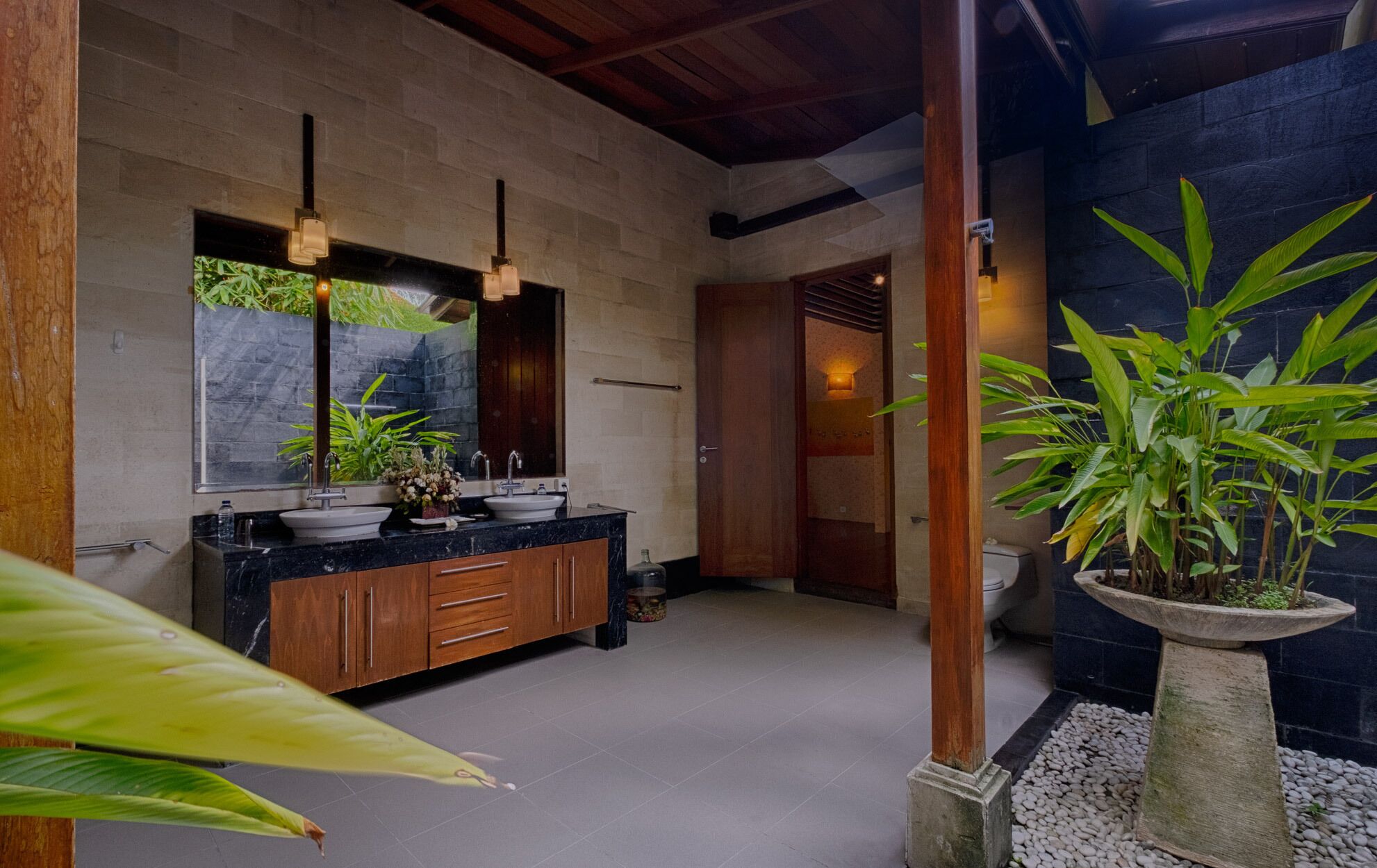 Une salle de bain moderne avec un grand miroir, deux vasques, des meubles en bois et une plante en pot.