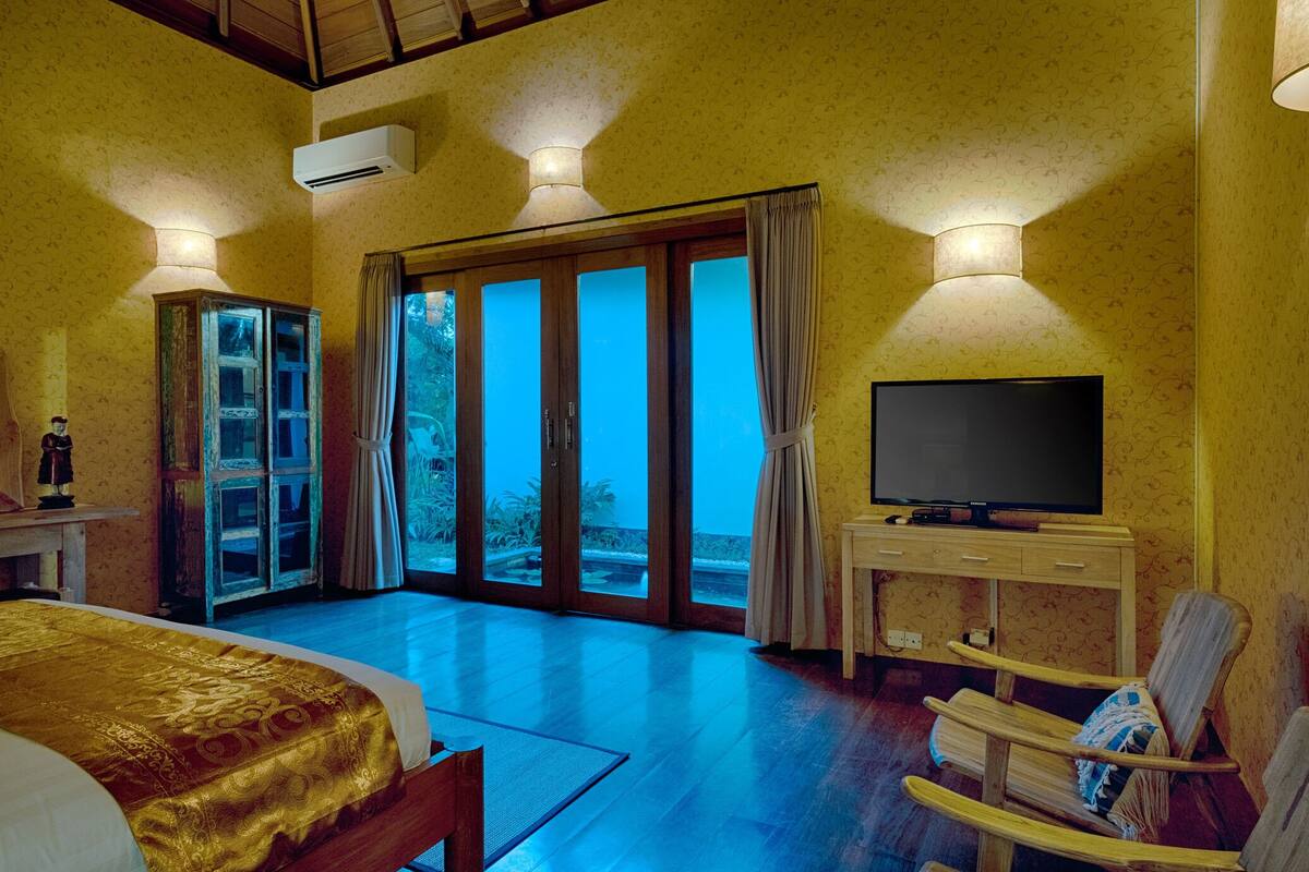 Een hotelkamer met een bed, een televisie, een houten stoel, een kast en een glazen schuifdeur naar een buitenruimte.