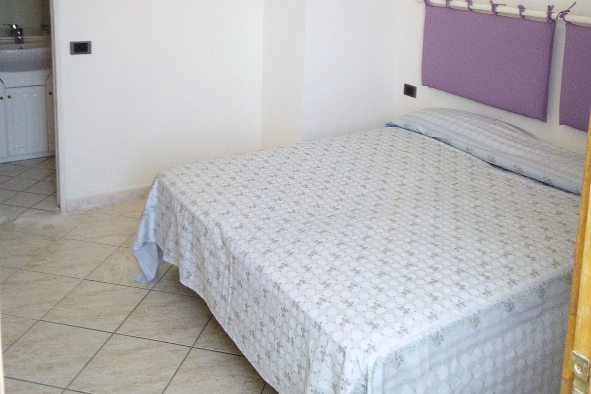 Un dormitorio con cama, cabecera y baño a la vista.