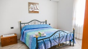 A bedroom with a metal bed frame, a blue patterned bedspread, a small wooden nightstand, and a painting on the wall. - Terra Mia (Agerola)