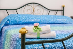 A bed with a blue patterned bedspread, a neatly folded white towel with a pink flower, and a brass bed frame. - Terra Mia (Agerola)