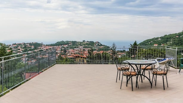 A terrace with a table and chairs, offering a view of a town with red-roofed buildings and greenery. - Terra Mia (Agerola)