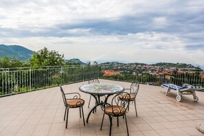 A terrace with a round table and four chairs, a sun lounger, and a view of a town and mountains. - Terra Mia (Agerola)