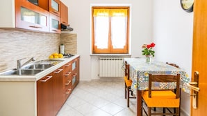A compact kitchen with a dining area, featuring a window with curtains, a sink, and a table with chairs. - Terra Mia (Agerola)