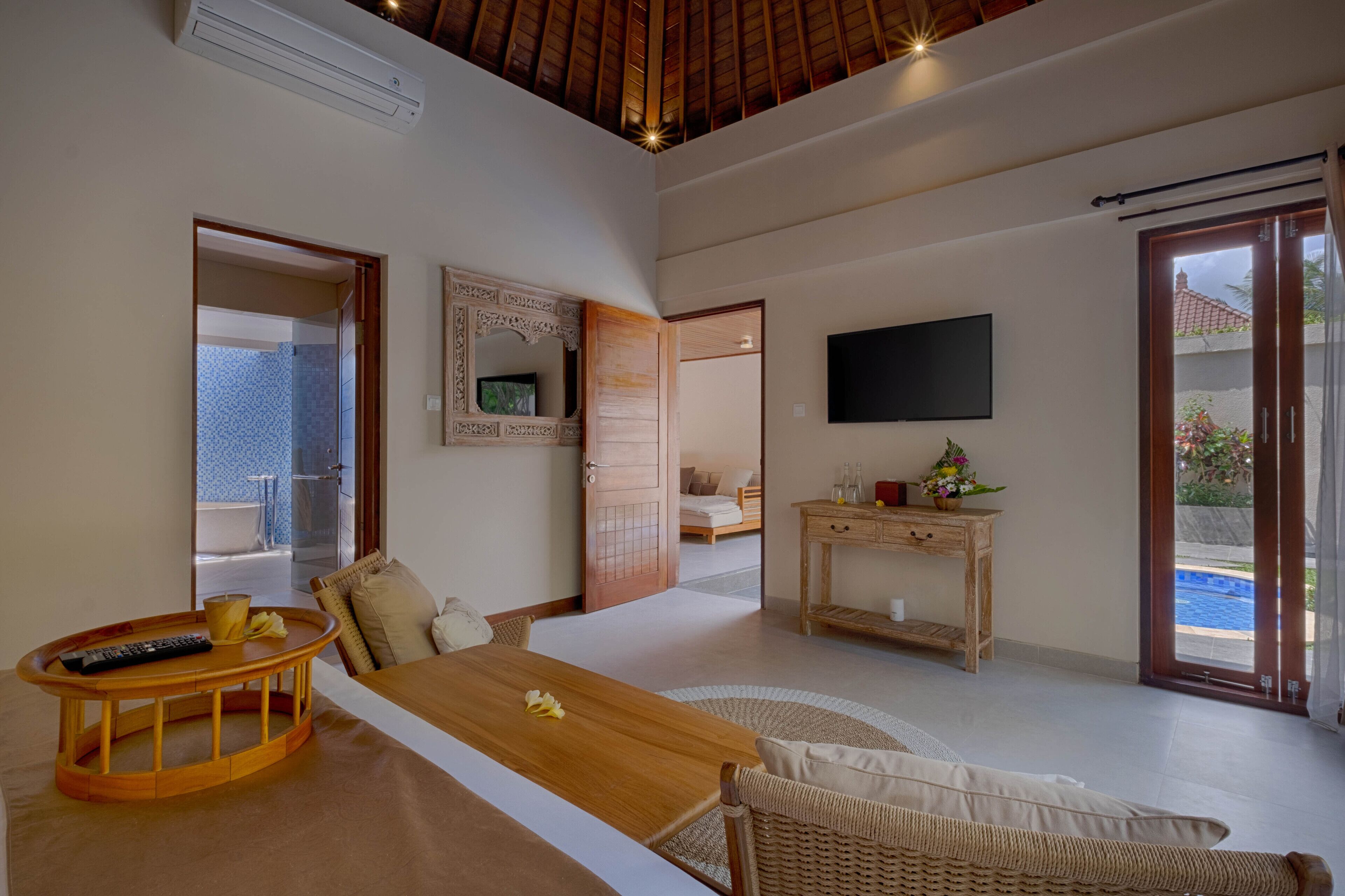 A spacious room with a wooden dining table, a TV mounted on the wall, and a sliding glass door leading to an outdoor area.