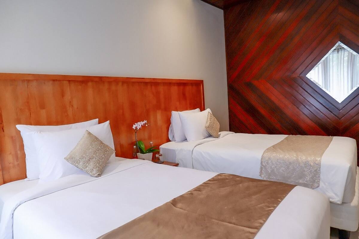 Quarto de hotel com duas camas, cabeceira de madeira e parede com padrão único em tons de vermelho e castanho.