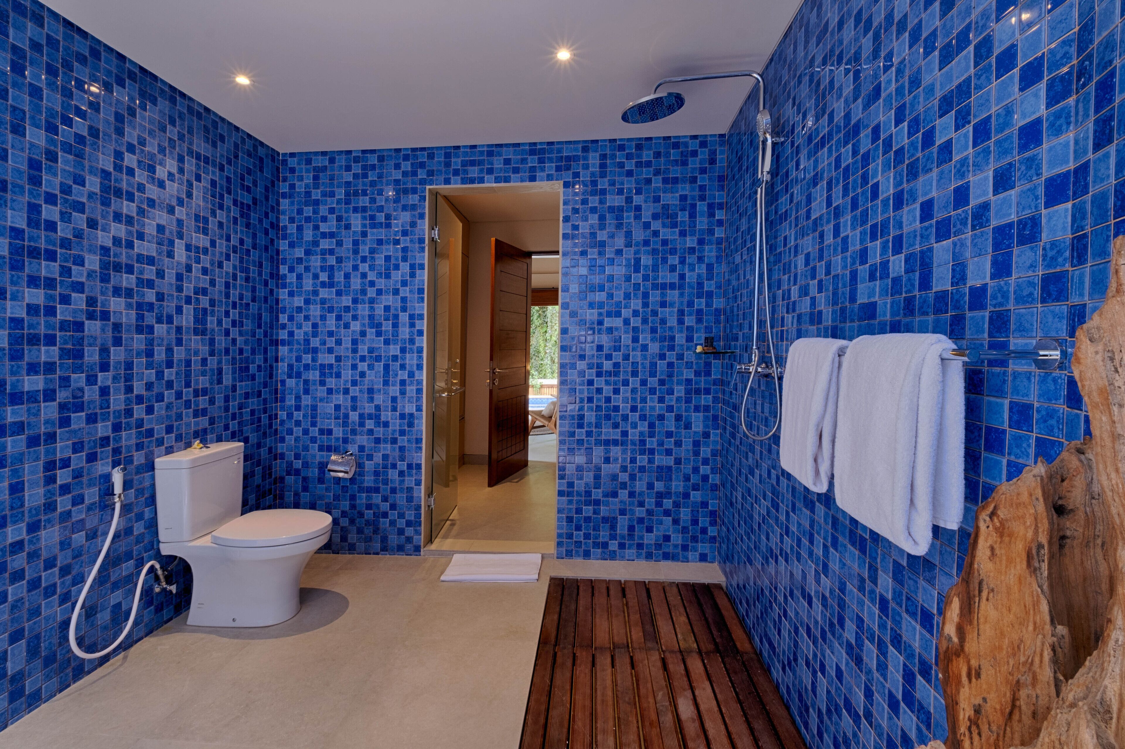 A bathroom with blue mosaic tiles, a toilet, a shower, and a towel rack.