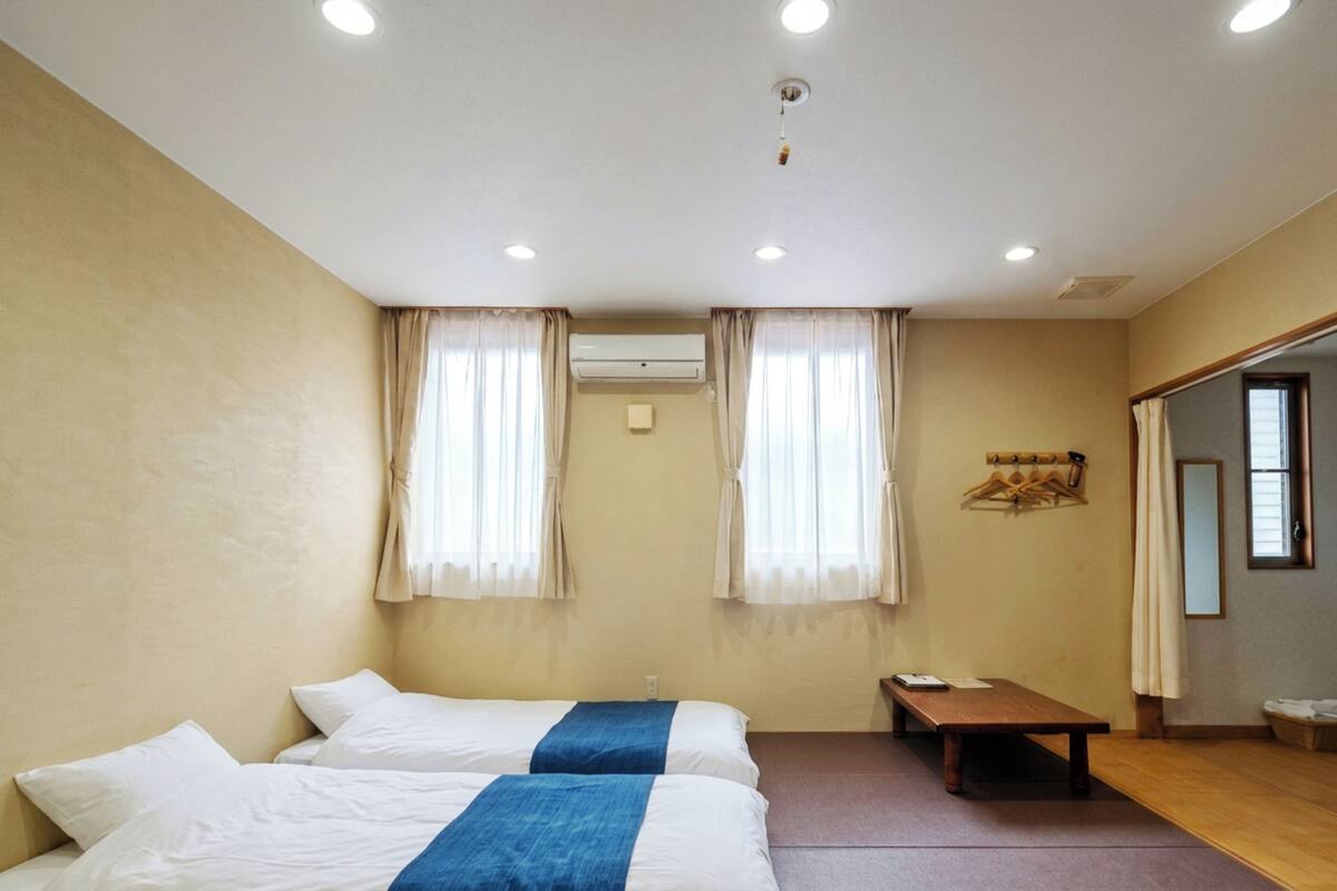 A hotel room with two beds, a small table, and a bench.