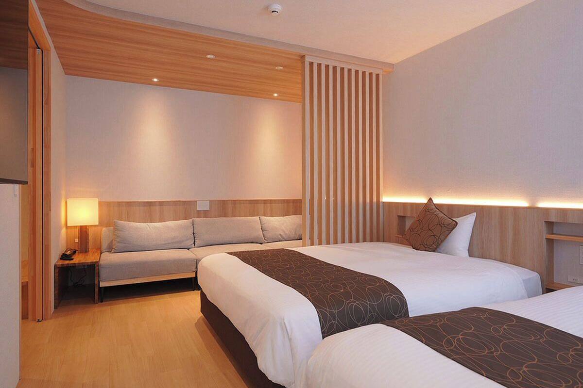 A hotel room with two beds, a sofa, a desk, and a lamp.